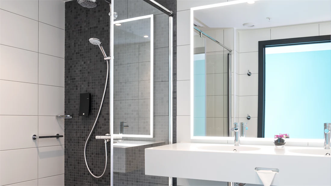 Stor åpen dusj med god gulvplass og lysegrå fliser på gulvet på badet i business og handikaprom på Thon Hotel Storo i Oslo