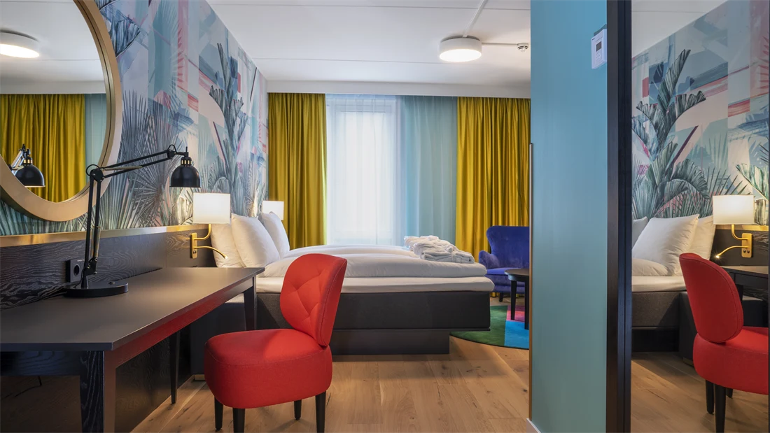 Skrivebord, rød stol, speil og dobbeltseng i superior HCP rom på Thon Hotel Storo