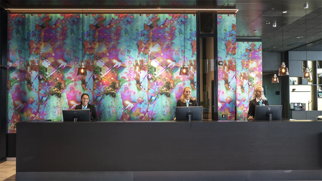 Resepsjonister bak resepsjonsdisk med fargerik tapet på Thon Hotel Storo