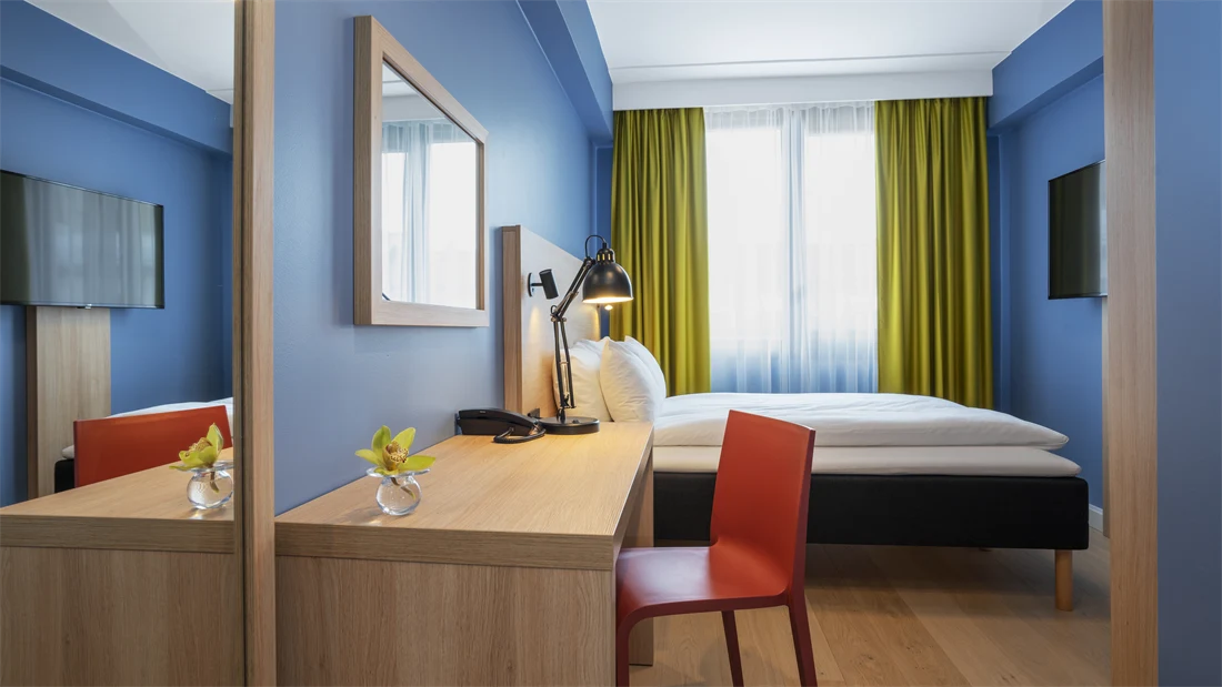 Speil. skrivebord med rød stol, blå vegger, dobbeltseng og gule gardiner i dobbeltrom på Thon Hotel Astoria