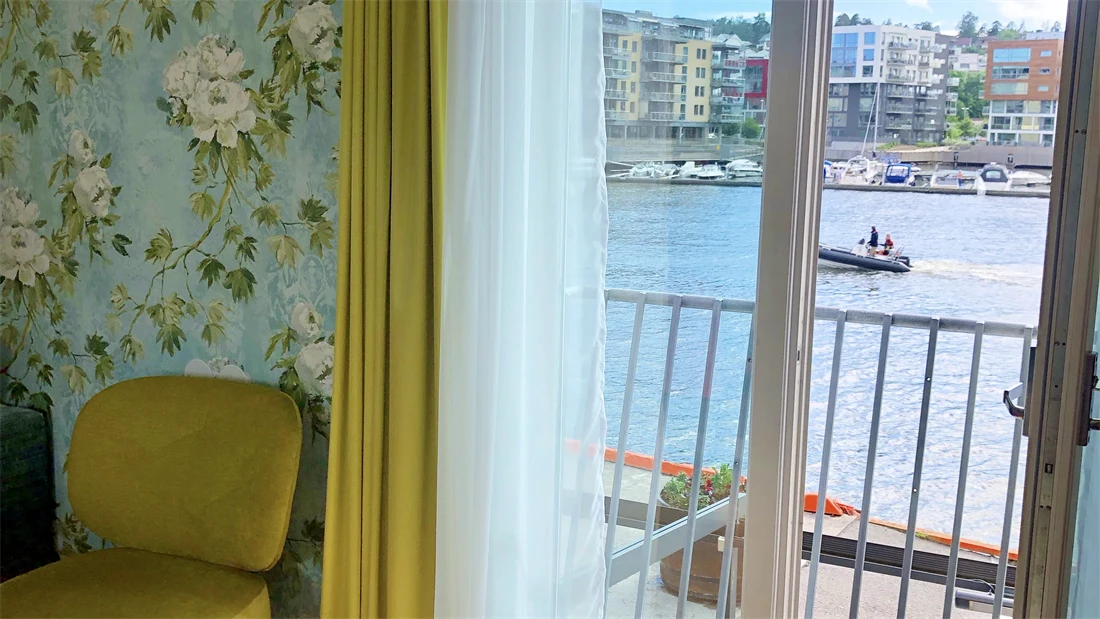 Rom hos Thon Hotel Tønsberg Brygge med gulv til tak-vindu, mønstrete tapet, gul stol og parkettgulv.
